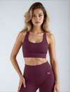 Woman wearing a burgundy sports bra and leggings with a logo on a plain background
